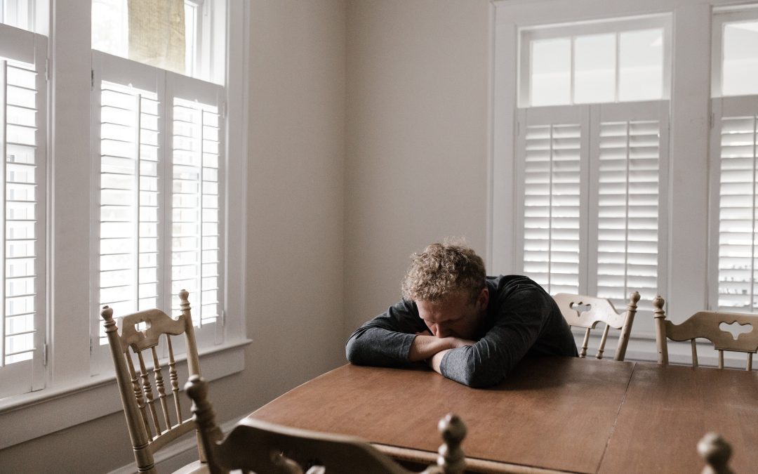 A man sits at a table looking depressed with his head on the table, he may be in a coercive co-parenting relationship