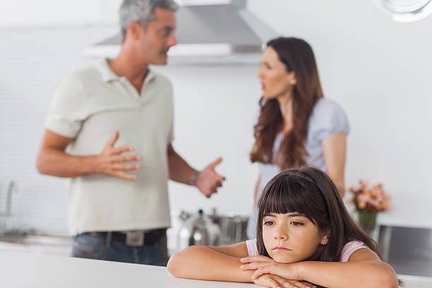 Young girl looks sad as divorcing parents argue behind her and unable to make child arrangements